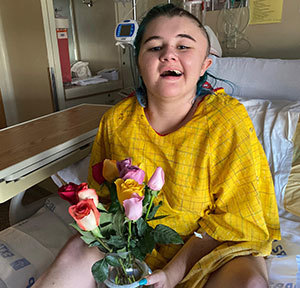 Megan holding bouquet of flowers and sitting on Craig inpatient bed